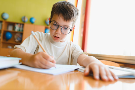 Young student wearing eyeglasses writing on notebook with pencil, studying at desk in classroomの写真素材
