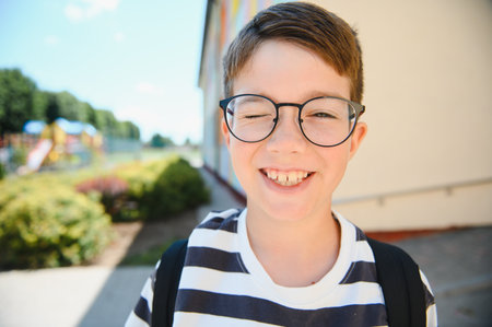 Winking boy enjoying back to school excitement near school, radiating happiness and cheerfulness as he embraces new adventures aheadの写真素材