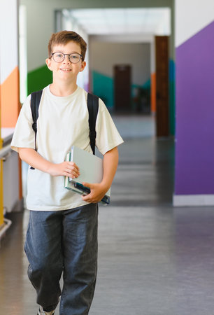 Confident student walking in school hallway, carrying books and backpack, ready for class, back to school conceptの写真素材