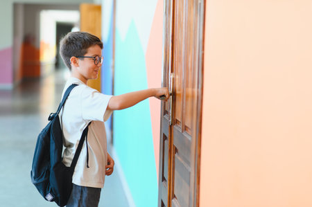 Smiling male student with backpack opening classroom door at school after summer holidays, back to school conceptの写真素材