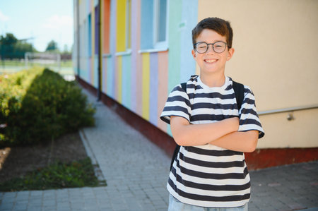 Portrait of a cheerful student standing with arms crossed in front of a vibrant school, exuding...