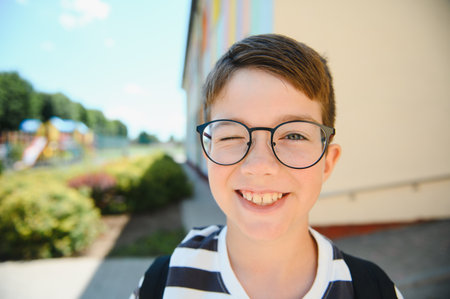 Portrait of a cheerful winking student wearing eyeglasses and backpack, enjoying his back to school dayの写真素材