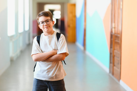 Portrait of a smiling student standing with arms crossed in a school hallway, ready for learning and academic successの写真素材