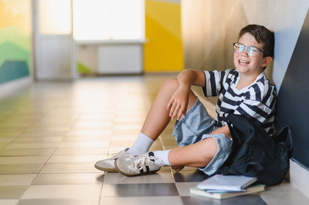 Schoolboy sitting on the floor of a school corridorの写真素材