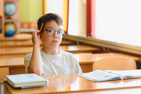 Elementary school student contemplating during a lesson, holding a pencil and engaging with educational material in a classroom settingの写真素材