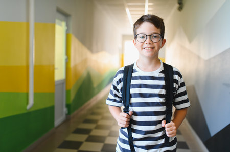 Portrait of a smiling male student wearing glasses and backpack walking in the school corridor during break timeの写真素材