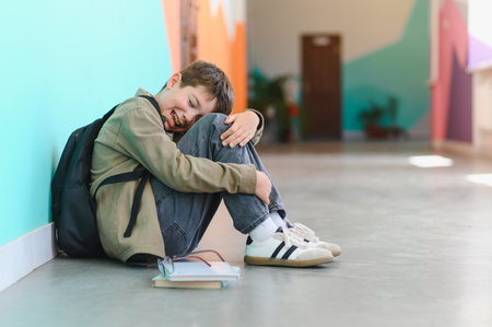 Sad schoolboy sitting on floor with backpack and books, crying after suffering bullying at school
