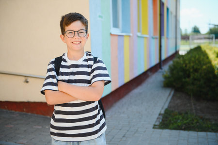Portrait of a cheerful student standing with crossed arms in front of a vibrantly colored school,...