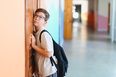 Elementary school student with backpack listening at classroom door, experiencing back to school anxiety in school hallwayの写真素材