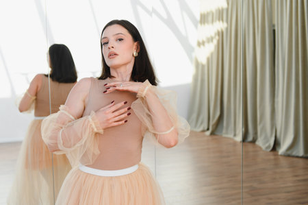 Young woman in ballet costume posing gracefully in a dance studio, reflected in a large mirror, showcasing elegance and poiseの写真素材