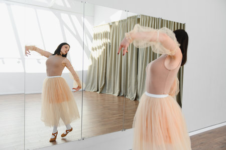 Young woman with peach tutu practicing ballet moves in a dance studio, using a mirror to perfect her techniqueの写真素材
