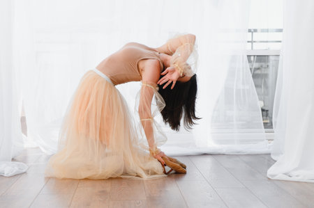 Young woman ballerina wearing tutu and leotard, kneeling on wooden floor and bending backwards in dance studioの写真素材