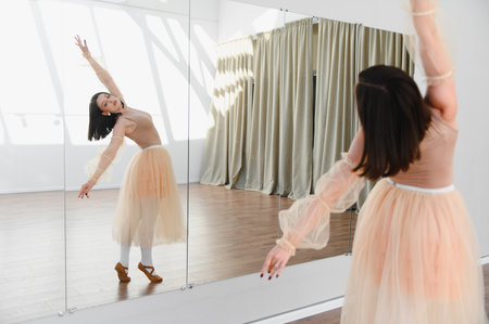 Young ballerina practicing ballet moves in a dance studio, wearing a tutu and leotard, with a mirror reflecting her graceful movementsの写真素材