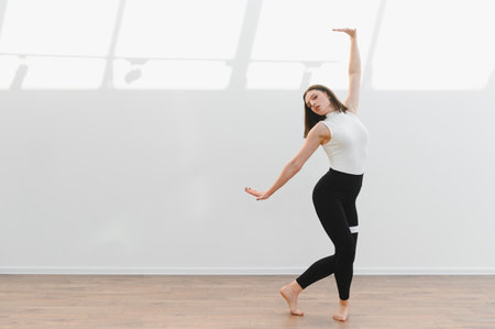 Dance student practicing a modern choreography in a luminous studio with wooden floor and white wallsの写真素材
