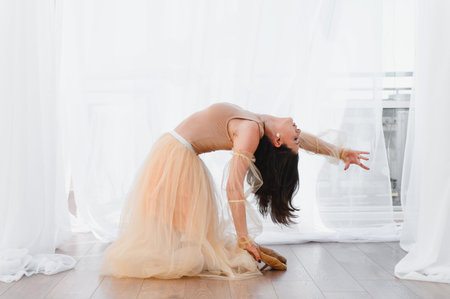 Young woman ballerina wearing a tulle skirt performing a backbend dance pose in a bright dance studioの写真素材