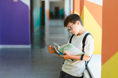 Young student reading a book in the school hallway, focused on learning and knowledge during break timeの写真素材