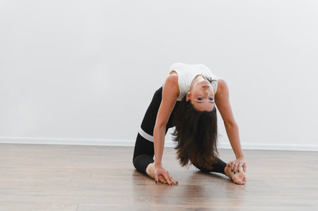 Flexible female dancer practicing a backbend stretch, showcasing her skills and dedication to contemporary dance in a bright studioの写真素材