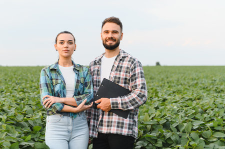 Two farmers are standing in a soybean field, holding a clipboard and inspecting the growth of their...