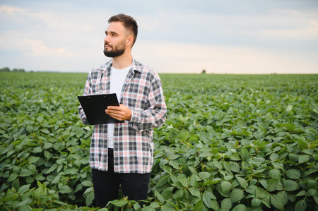 Agronomist inspecting soybean plants and taking notes on a clipboard in a large cultivated field