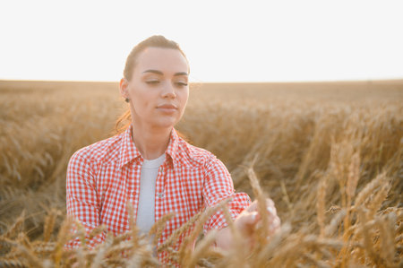 Young woman farmer gently touching ripe wheat ears in a cultivated agricultural field, basking in...
