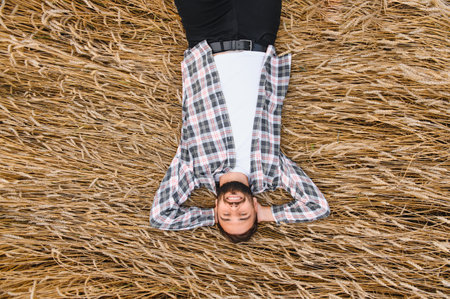 Farmer lies in a wheat field, hands behind his head, enjoying a moment of peace after the harvestの写真素材