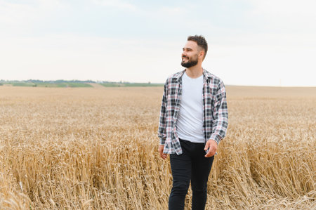 Young farmer walking through a golden wheat field, savoring the joys of harvest while smiling under the warm summer sunsetの写真素材