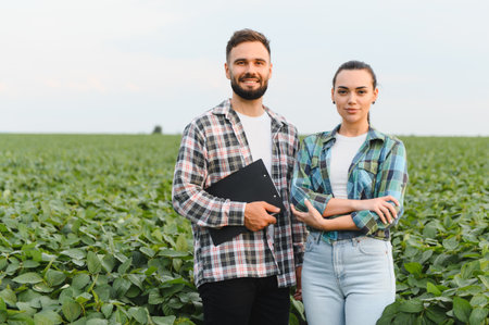 Two confident farmers are standing amidst a lush soybean field, one holding a clipboard, showcasing...