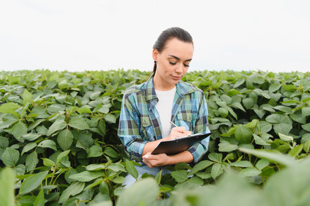 Female agricultural engineer examining crops and taking notes on a clipboard in a soybean field