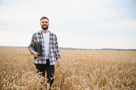 Happy farmer walking through a vibrant wheat field, holding a laptop and smiling joyfully while embracing modern agricultural technologyの写真素材