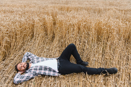 Happy farmer is lying down in his wheat field after a successful harvest, enjoying the fruits of his laborの写真素材