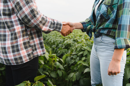 Two farmers shaking hands in cultivated soybean field, celebrating successful harvest and...