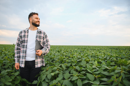 Agronomist inspecting growing soybean crops in a lush field, holding a clipboard while thoughtfully gazing into the distanceの写真素材