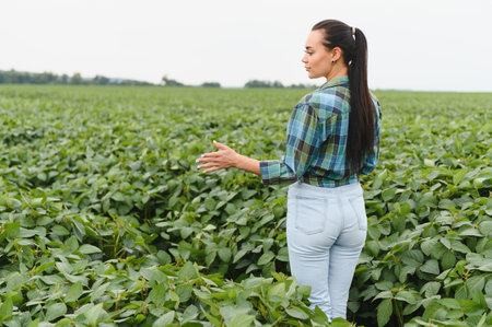 Young woman farmer inspecting the growth of soybean plants in a cultivated field, ensuring a healthy and productive harvestの写真素材