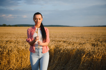 Young female farmer examining a stalk of wheat in a golden field, enjoying the fruits of her labor...