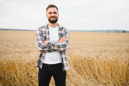 Portrait of a confident farmer smiling with arms crossed, standing in a golden wheat field, enjoying a successful harvest seasonの写真素材