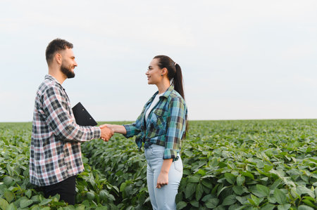 Two farmers shaking hands in a soybean field, celebrating a successful business agreement in the...