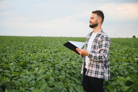 Agronomist examining plants in soybean field, holding clipboard and taking notes, assessing growth...