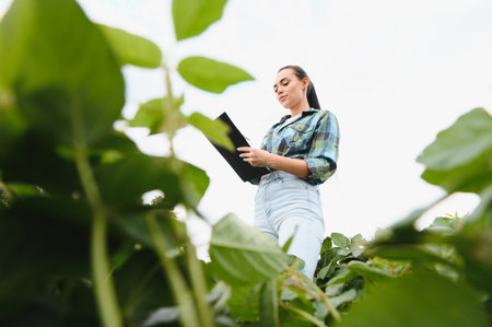 Female farmer analyzing the growth of her soybean plants, holding a clipboard and taking notes...