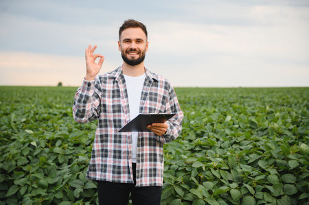Agronomist holding a clipboard and making an 'ok' gesture while inspecting healthy soybean crops in a lush, green fieldの写真素材