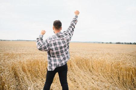 Farmer with raised arms celebrating a successful harvest in a golden wheat field, expressing joy and gratitude for nature's bountyの写真素材