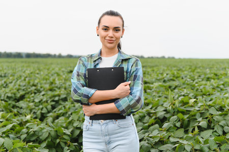 Confident female agronomist holding clipboard, standing amidst lush soybean plants, ensuring healthy...