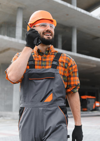 Construction worker wearing hard hat and safety glasses, using a walkie talkie for communication on...
