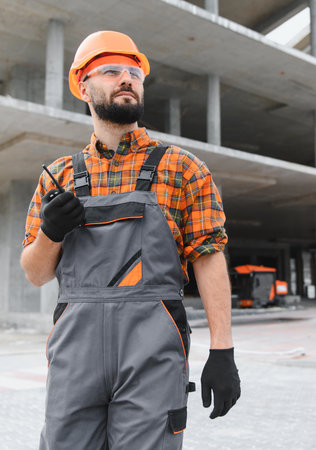 Construction worker wearing hard hat and safety glasses, communicating with walkie talkie on a...