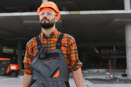 Construction worker in hard hat and safety glasses at a building site, focused and professional,...