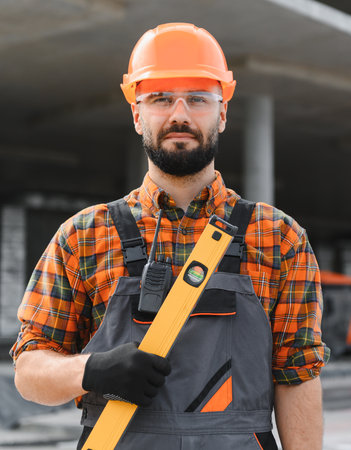 Worker in safety gear holding a spirit level, ready for work on a construction site. Representing building and developmentの写真素材
