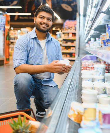 Customer holding yogurt, selecting groceries in refrigerated section of modern supermarket, making healthy food choicesの写真素材