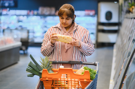 Young woman pushing shopping cart and choosing cheese in a supermarket groceries dairy sectionの写真素材