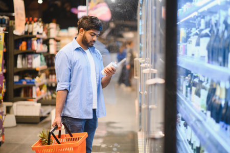 Focused customer reading label on refrigerated product in grocery store, holding shopping basket with pineappleの写真素材