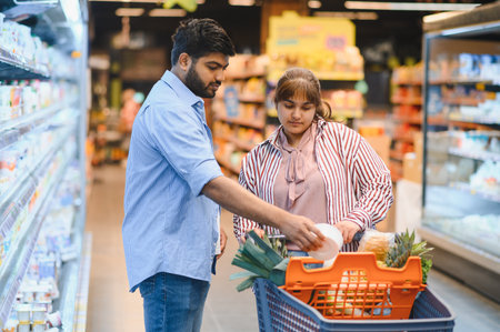 Indian couple selecting fresh produce and groceries in a vibrant supermarket, happily adding items to their shopping cart togetherの写真素材