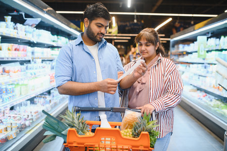 Young Indian couple checking their shopping list while selecting fresh groceries together in a...